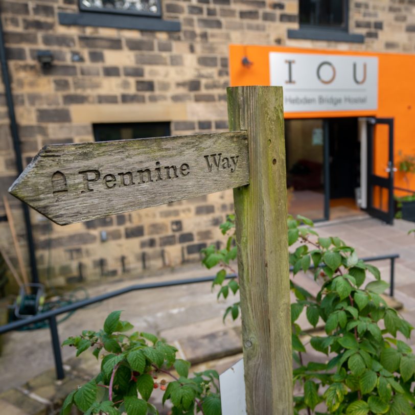 Building with orange frontage in background. In foreground is a way finding sign for the Pennine Way