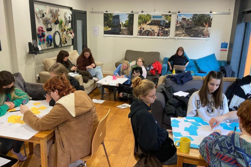 large group of students work in groups in large space with posters on the wall